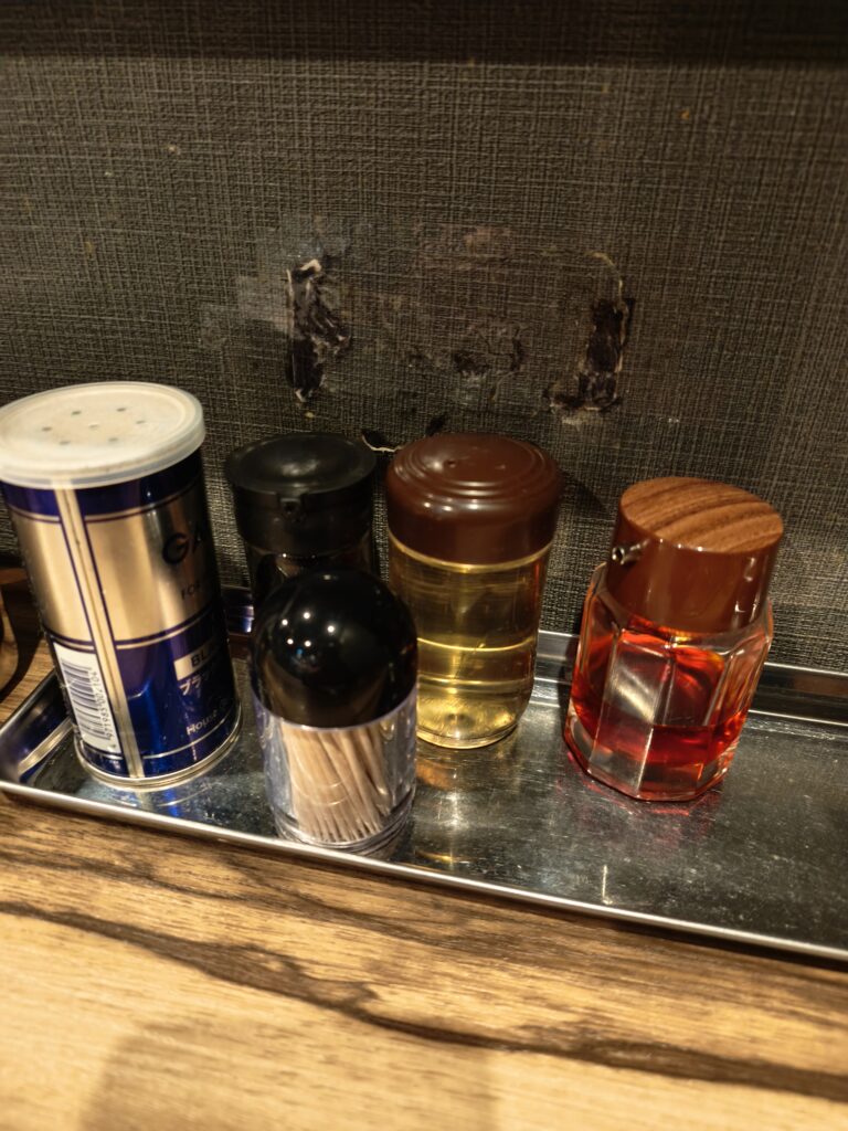 石川家大宮店の卓上に用意された、ニンニクや豆板醤、生姜などの豊富な調味料