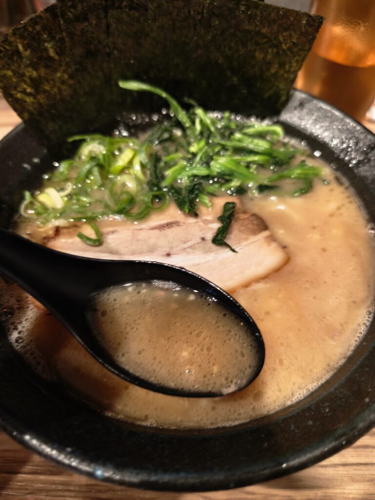 石川家大宮店のラーメンの、鶏油が浮かぶ濃厚な豚骨醤油スープをレンゲですくった様子